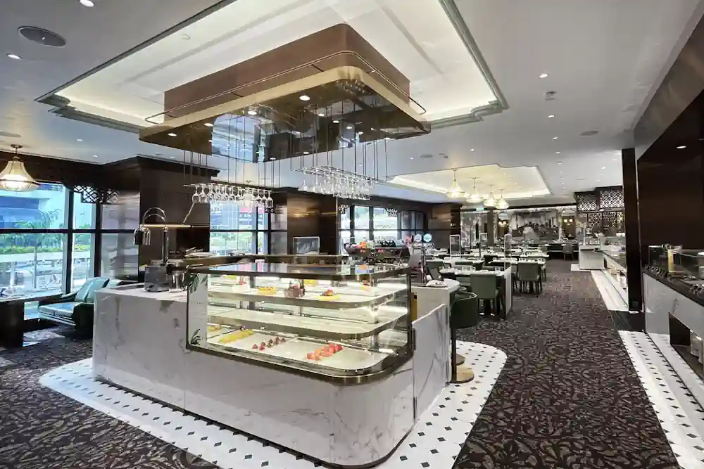 香港六國酒店自助晚餐餐廳的內部環境，設有雅緻的綠色座椅和水晶吊燈，自助餐區在右側，展現舒適的灣仔餐飲氛圍