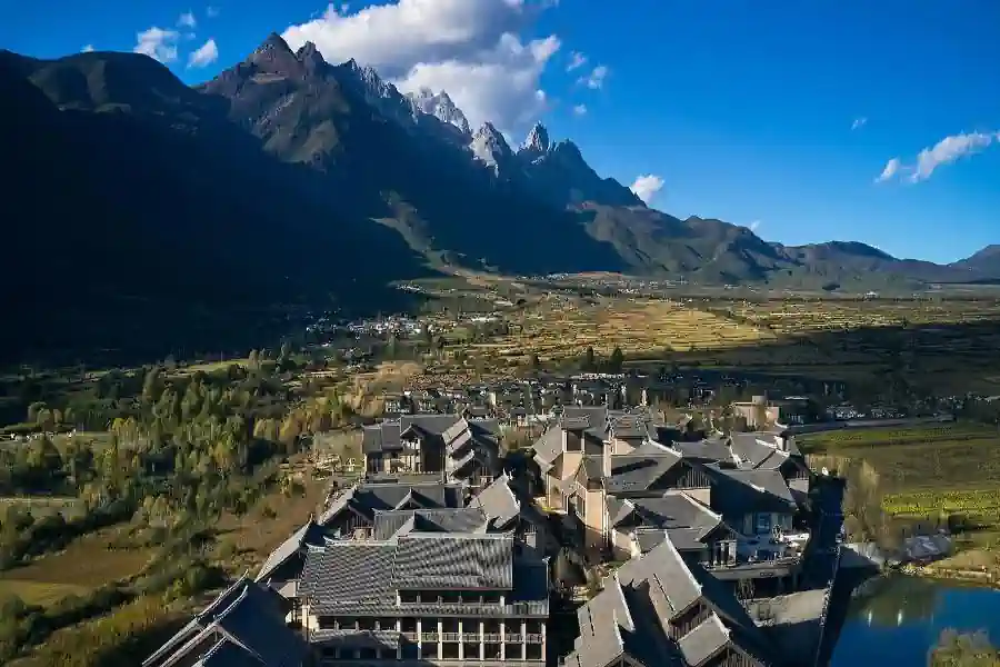 麗江 Club Med 度假村航拍全景，背景是雄偉的玉龍雪山，建築群融合了納西族傳統風格。